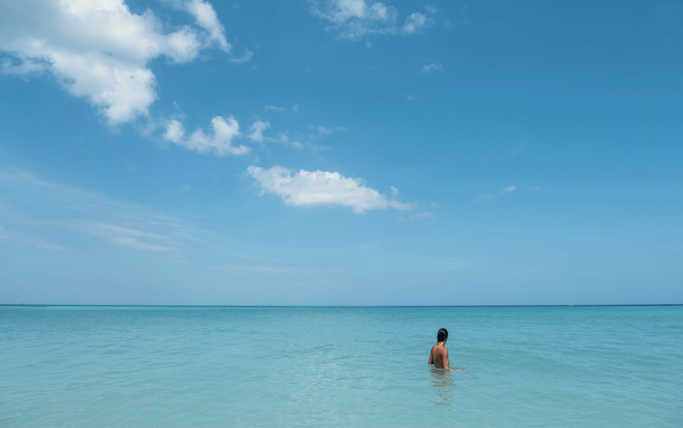 A lone swimmer in turquoise water under a wide blue sky